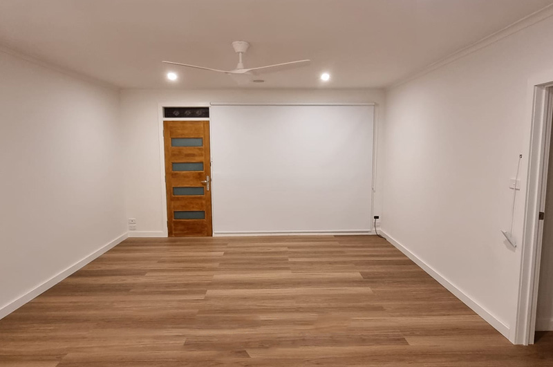 After: empty living room with timber-look flooring, downlights and a ceiling fan