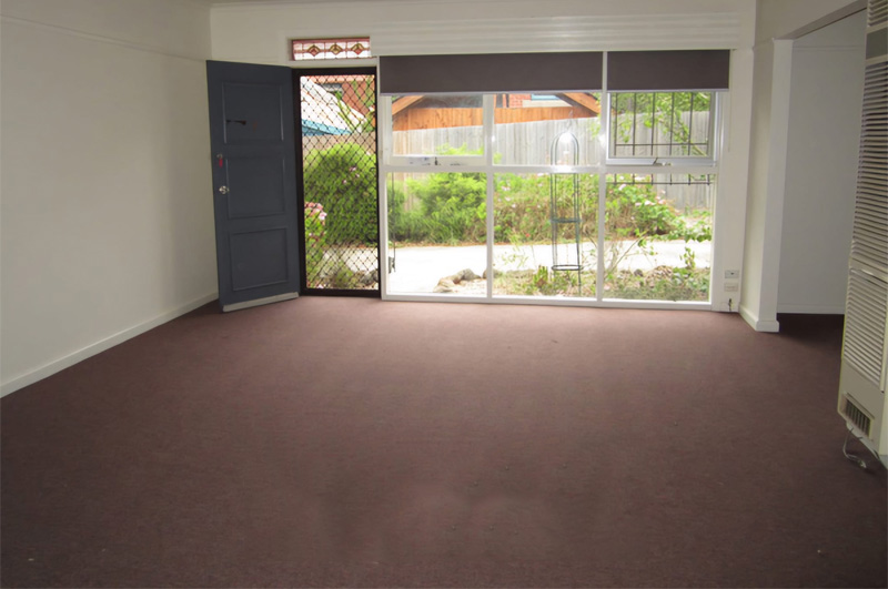 Before: empty living room with dark carpet and a sliding door to the garden