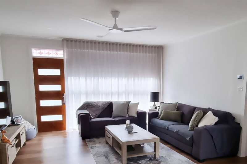 After: living room with timber-look flooring, sheer curtains and grey sofas