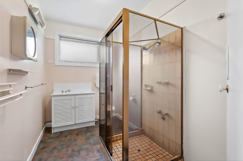 Before: dated bathroom with a gold-framed shower screen and vinyl floor