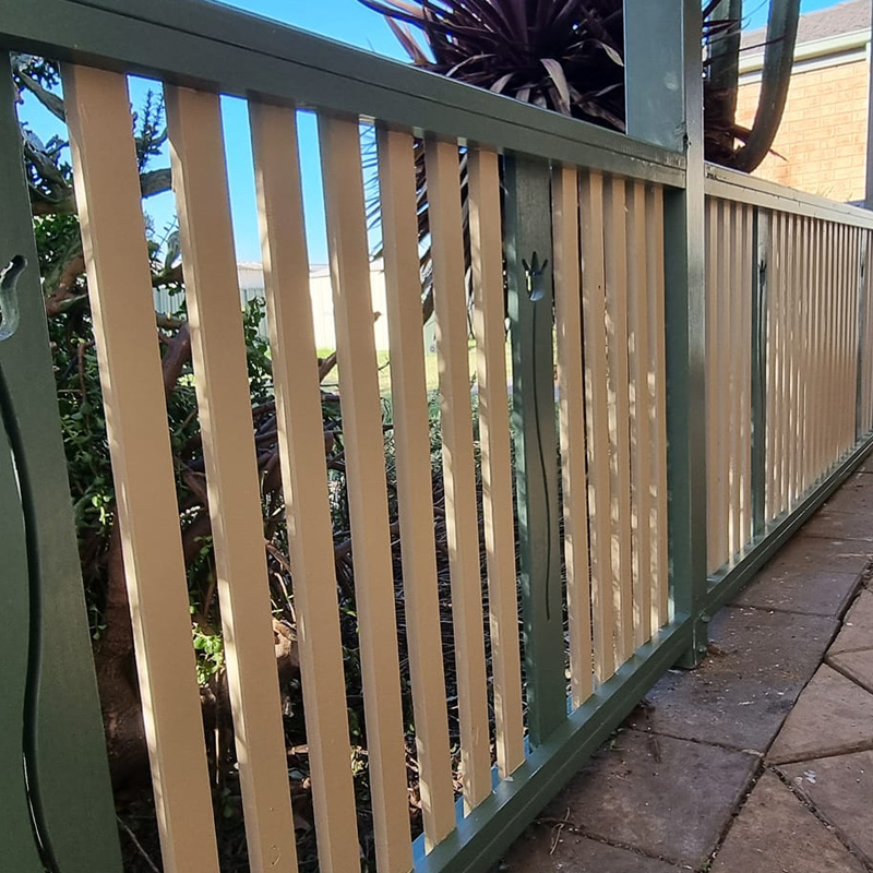 Timber slats fitted in a green metal fence frame beside a paved path