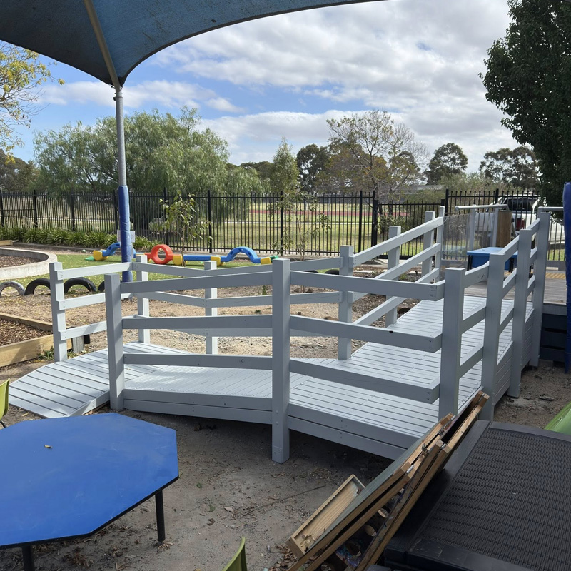 Grey painted timber ramp with railings under a shade sail in a play area