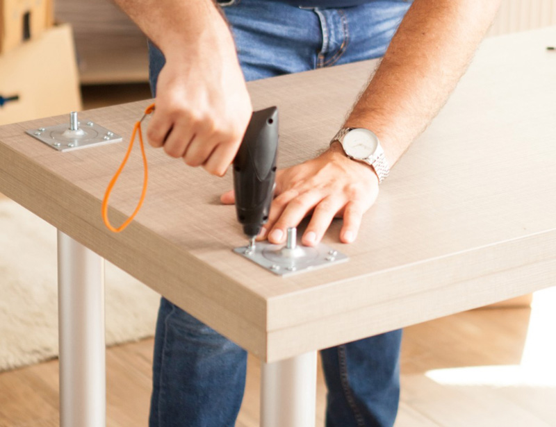 Person screwing leg mounting plates onto a desk top with a cordless screwdriver