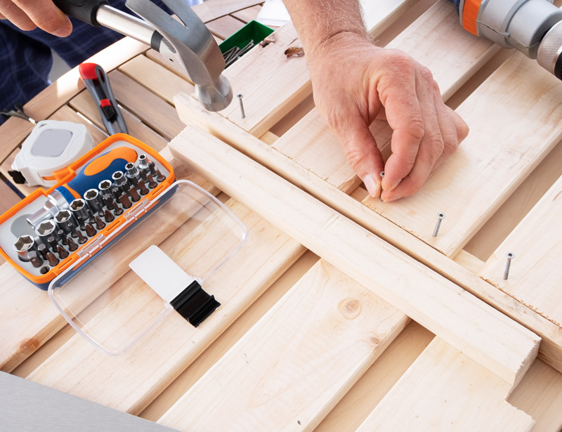 Hammer, screwdriver bit set and screws on pine boards being assembled