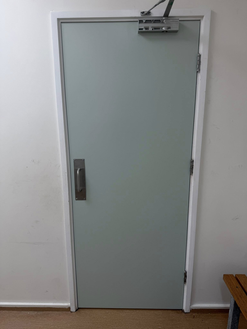 Pale green door with a door closer in a white wall