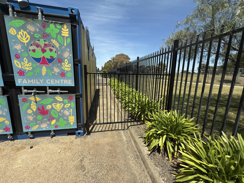 Black steel fence and gate beside a container with a Family Centre mural