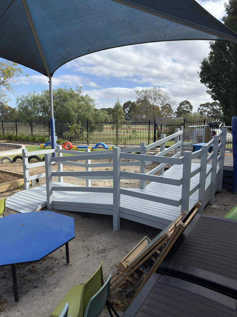 Grey painted timber ramp with railings under a shade sail in a play area