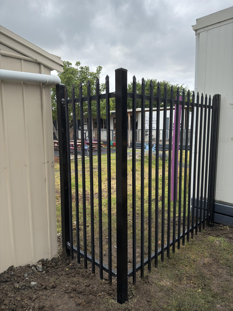 Black steel fence panel and gate between two buildings