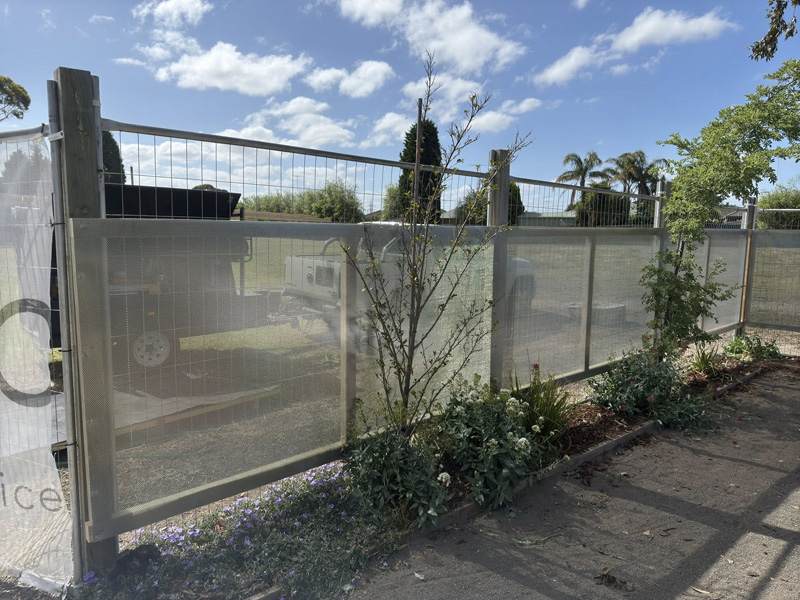 Fence with frosted screen panels and mesh above, beside a garden bed