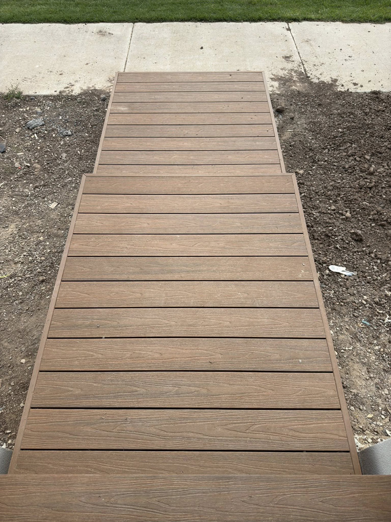Brown decking path with steps across bare soil from the footpath