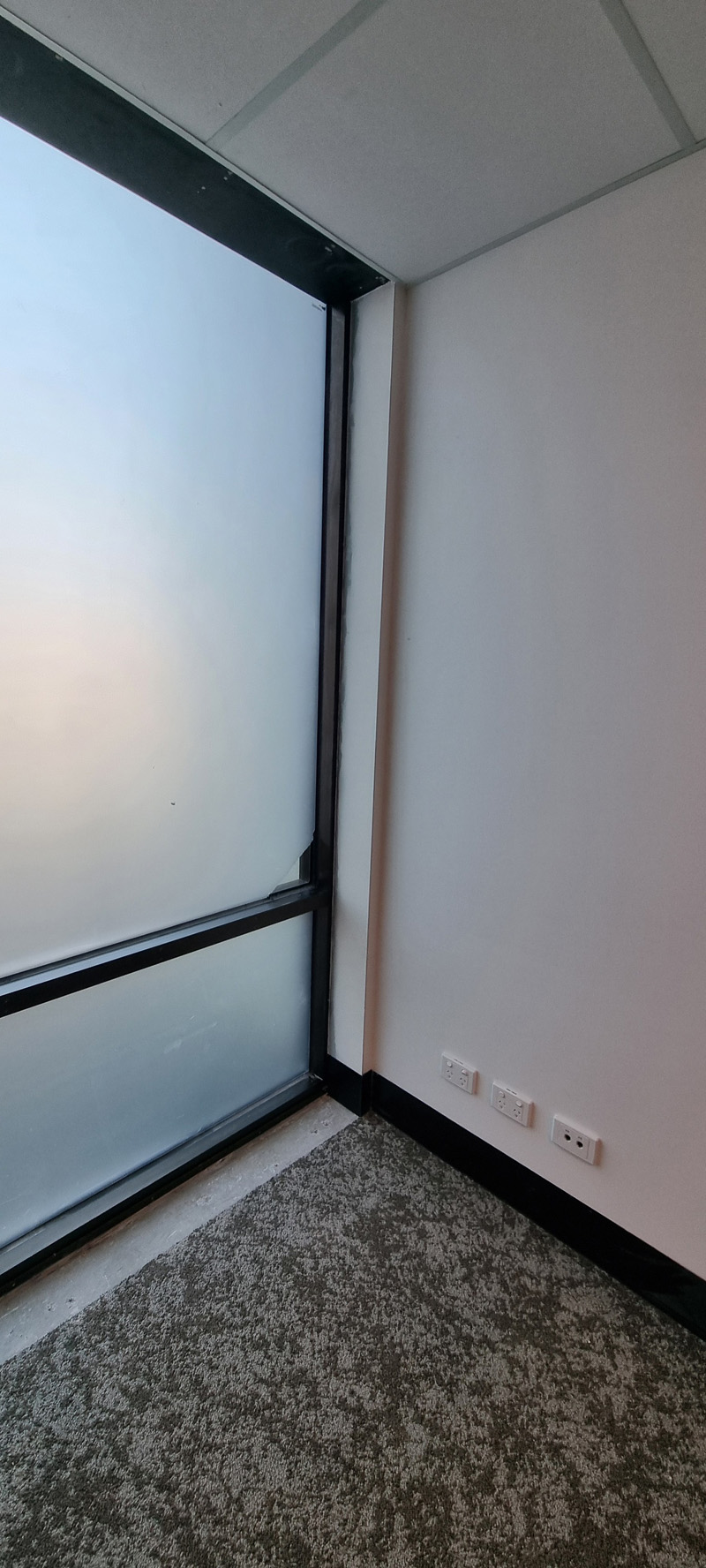 Room corner with a frosted floor-to-ceiling window and speckled carpet