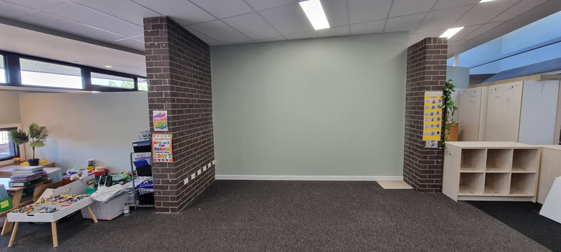 Room with a pale green painted wall between brick piers and dark carpet