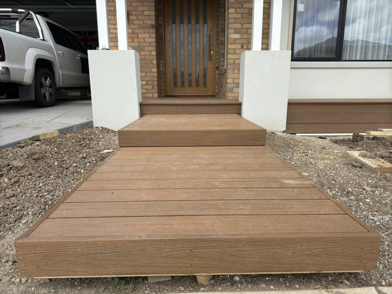 Timber decking path and step to a brick home's front door beside a carport