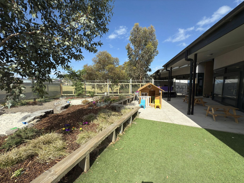 Timber garden bed edging beside artificial grass in a play area with a cubby house