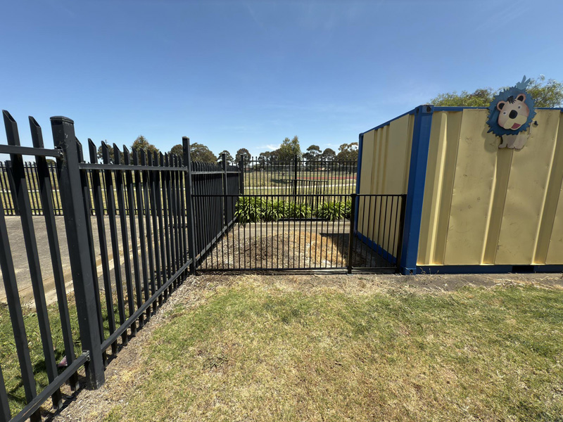 Black steel fence and gate beside a yellow shipping container